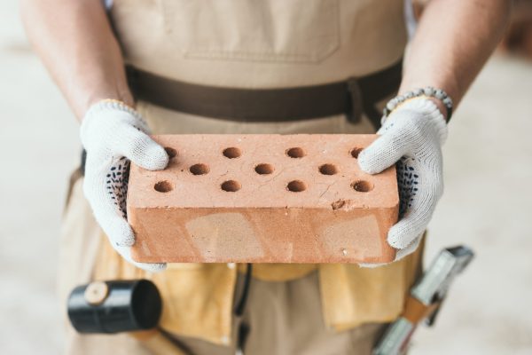 cropped image of builder in protective gloves holding brick